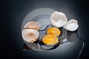 Raw smashed chicken eggs with yolks, proteins and eggshell on black background.