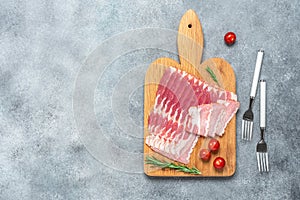 Raw smoked bacon slices on a wooden cutting board. Gray concrete background. Top view, flat lay, copy space