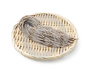 Raw soba noodles in a bamboo colander placed against a white background