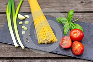 raw spaghetti decorated with spring onions, basil, tomatoes and garlic