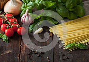 Raw spaghetti pasta in glass bowl with oil and garlic, basil and tomatoes with pepper and onion on wooden background