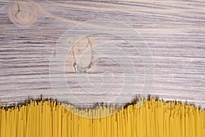 raw spaghetti pasta scattered on wooden table, close-up view from above