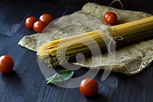 Raw spaghetti, red cherry tomatoes and green leaves with sackcloth on a wooden table