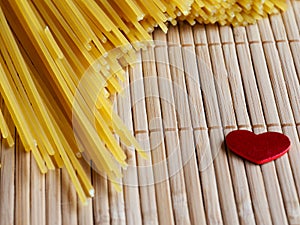 Raw spaghetti with red heart on a bamboo bakground