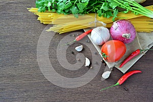 Raw spaghetti with tomato, garlic, onion and pepper, ingredients on brown wooden table.