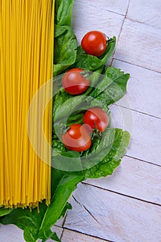 Raw spaghetti with tomatoes stand on spinach leaves on a white wooden table