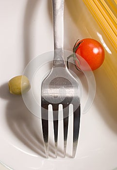 Raw spaghettis, tomato and olive with fork