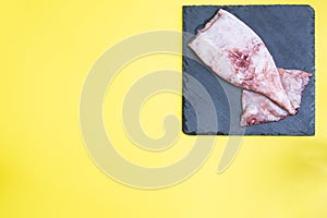 Raw squid carcass with spices on a black slate board. copy space Top view. Yellow background