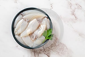 Raw squid fillet in a bowl over marble background. Small calamary tubes prepared for cooking. Fresh squid molluscs ingredient for