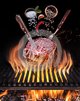 Raw Steak cooking. Conceptual picture. Steak with spices and cutlery under burning grill grate