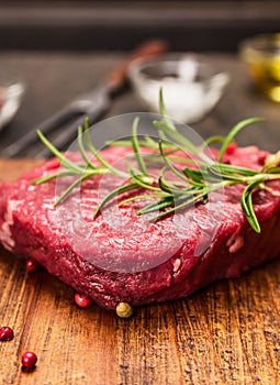 Raw steak on a cutting board with a fork, rosemary, salt and oil on rustic wooden background, close up