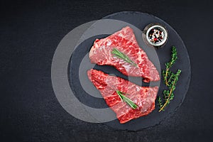 Raw steak on cutting board with rosemary and spices, dark black background, top view. Fresh grilled meat. Grilled beef
