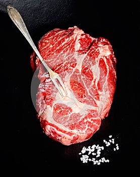 Raw steak from marble beef, salt, vintage meat fork on a black background