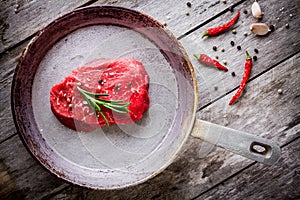 Raw steak in the pan with garlic and pepprs