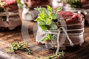 Raw steak wrapped with bacon and fresh herbs on a wooden cutting board
