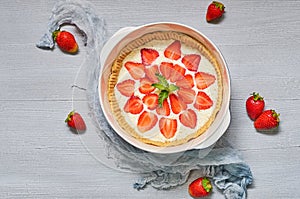 Raw strawberry tart on the gray kitchen background. Berries cheesecake decorated with organic fresh strawberries and mint