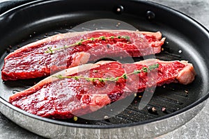 Raw strip loin steak on a grill pan, ingredients for cooking. Gray background. Top view