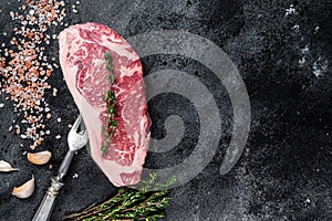 Raw striploin steak on a butcher table with salt and thyme. Black background. Top view. Copy space