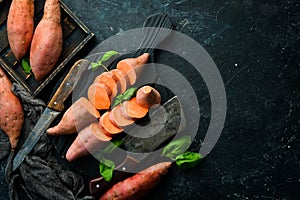 Raw sweet potatoes and basil on a black stone background. Top view.