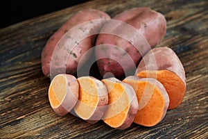 Raw sweet potatoes batatas on a rustic wooden table with black background