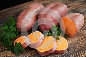 Raw sweet potatoes batatas on a rustic wooden table decorated with fresh parsley and dill