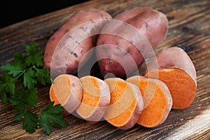 Raw sweet potatoes batatas on a rustic wooden table decorated with parsley
