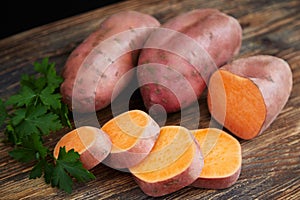 Raw sweet potatoes batatas on a rustic wooden table decorated with parsley