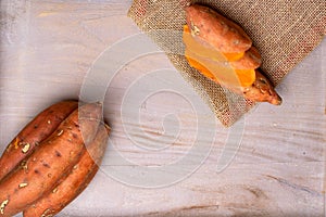 Raw sweet potatoes on wooden background in burlap sack