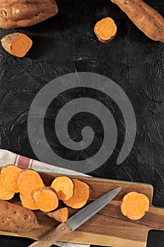 Raw sweet potatoes on wooden kitchen board top view