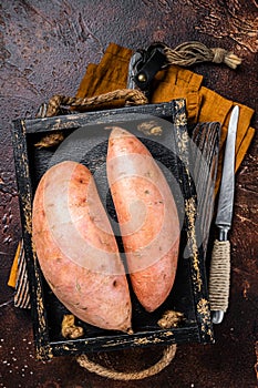 Raw sweet potatoes in a wooden tray, fresh batata. Dark background. Top view
