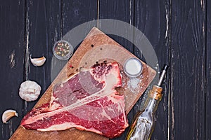 Raw T-bone beef steak on the wooden board and spices on black table.