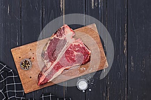 Raw T-bone beef steak on the wooden board and spices on black table.