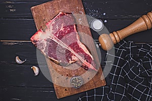 Raw T-bone beef steak on the wooden board and spices on black table.