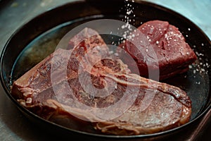 Raw T bone steak of beef meat in a frying pan against dark background. Selective focus.