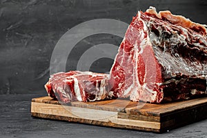 Raw T-bone steak cooking on stone dark table.