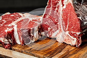 Raw T-bone steak cooking on stone dark table.