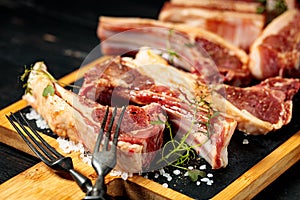 Raw T-bone steak and ribs on a black stone cutting board. Raw meat with spices and herbs. Close-up. Dark wooden background