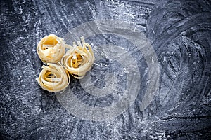 Raw tagliatelle nido on the flour-dusted black wooden background