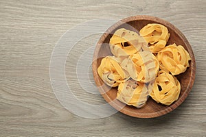 Raw tagliatelle pasta in bowl on light grey wooden table, top view. Space for text