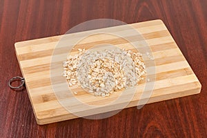 Raw thick-rolled oats on wooden cutting board on table