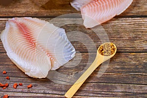 Raw tilapia fillets with seasonings over wooden background