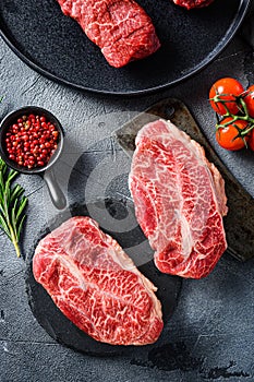 Raw top blade oyster Steak on stone and meat butcher cleaver, marbled beef with herbs tomatoes peppercorns over grey stone surface