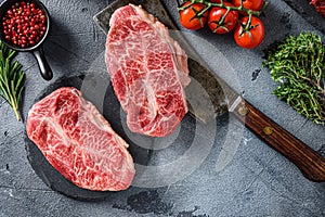 Raw top blade oyster Steak on stone and meat butcher cleaver, marbled beef with herbs tomatoes peppercorns top view