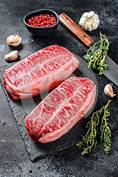 Raw top blade steak dry-aged on a stone board. Black background. Top view