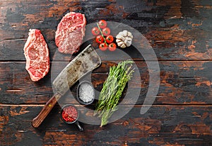 Raw top blade steaks with herbs seasoning and butcher knife over old dark wooden table top view, space for text