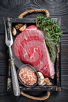 Raw top sirloin cap beef cut meat steak or Picanha in wooden tray with herbs. Black wooden background. Top view