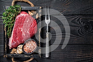 Raw top sirloin cap beef cut meat steak or Picanha in wooden tray with herbs. Black wooden background. Top view. Copy