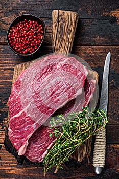 Raw top sirloin cap steak or Picanha steak on wooden board with thyme. Dark wooden background. Top view