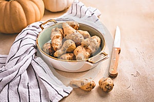 Raw topinambour with pumpkins in bowl on kitchen table