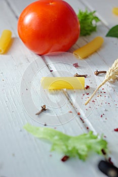 Raw Tortiglioni pasta with other ingredients over white wooden table.